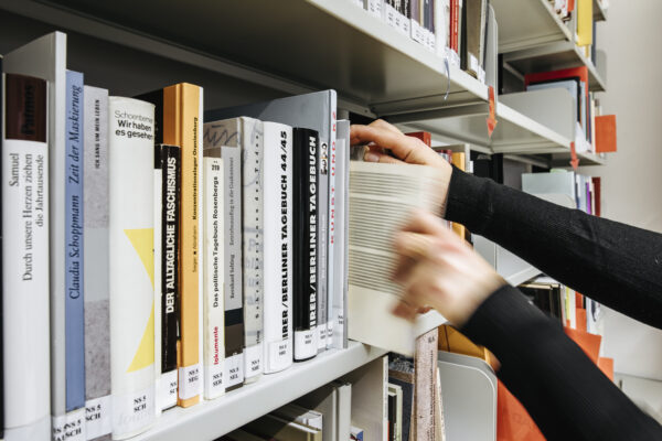 A bookshelf containing books on the history of National Socialism. A person is taking a book out of the shelf.