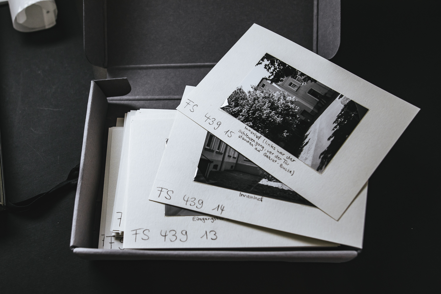 A cardboard box full of black and white photos that are glued to grey cardboard and bear an inscription.