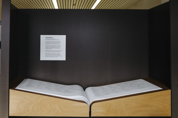 A large book lies open in a wooden frame, the writing of which is illegible. A sign above it reads "Memorial book", as translated.