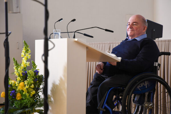 Ein Mann in einem Rollstuhl sitzt vor einem Rednerpult.