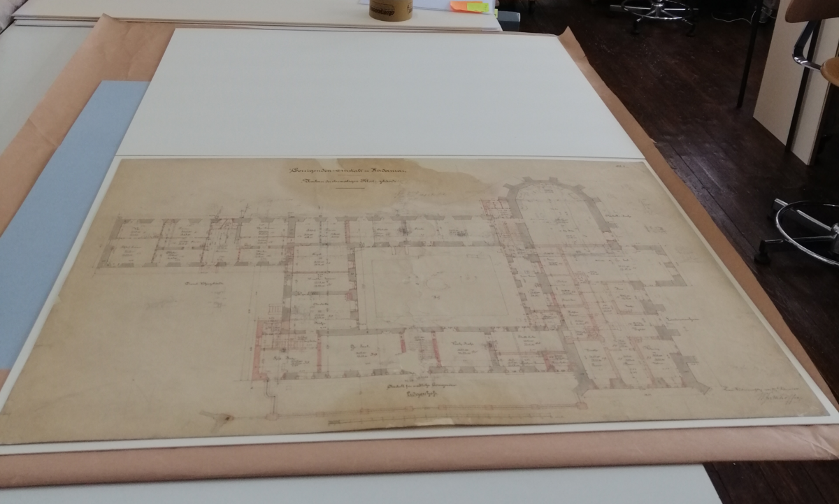 Ein vergilbter Gebäudeplan liegt auf einem weißen Tisch. bei genauerem Hinsehen sind die restaurierten Stellen am Plan zu erkennen.