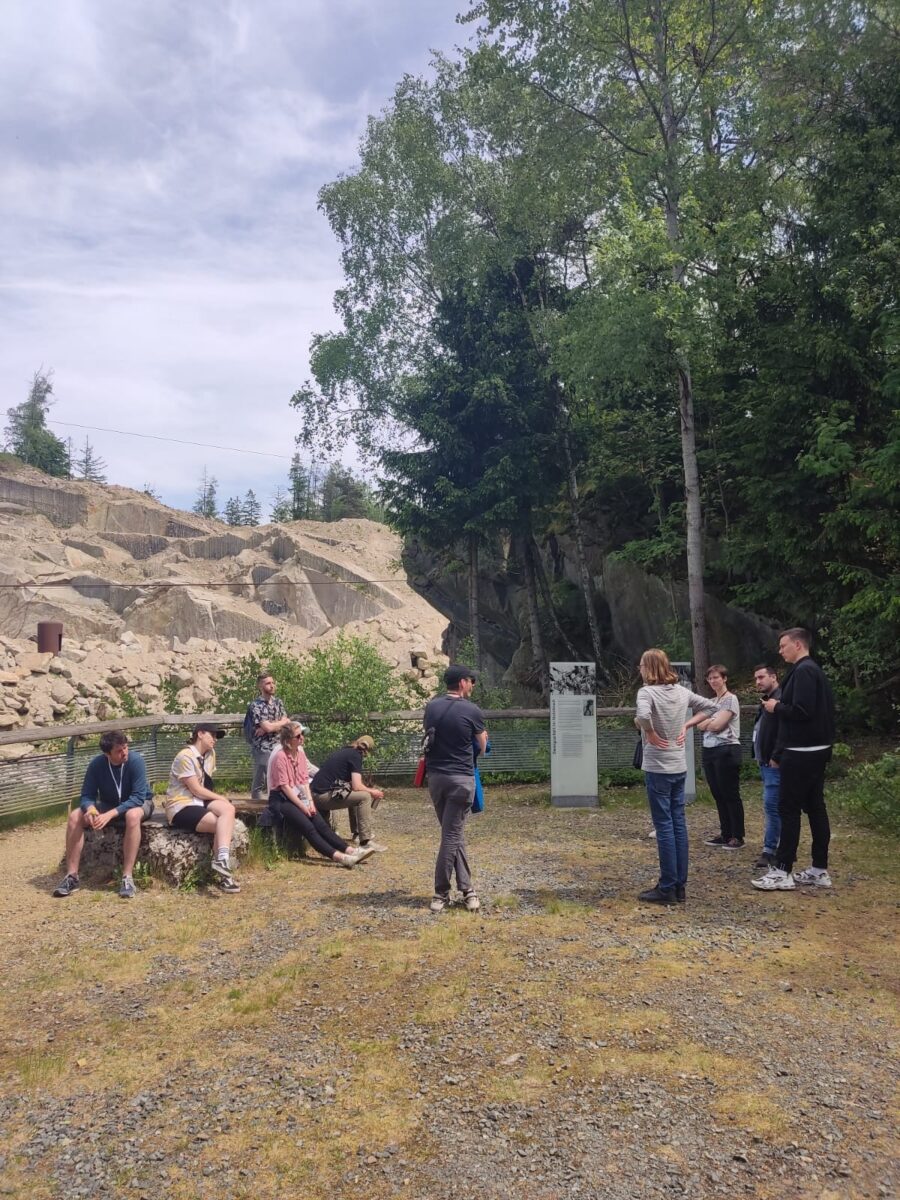 Eine Gruppe von Menschen steht vor einem alten Steinbruch, der mit einem Geländer abgegrenzt ist.