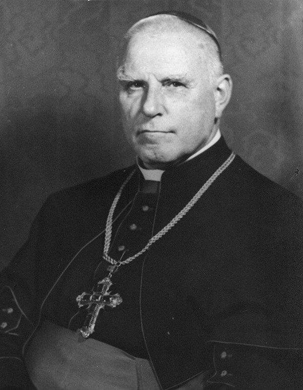 Ein schwarz-weiß Portrait von einem Bischof. Ein alter Mann schaut sitzend in die Kamera. Er trägt ein festliches Gewand mit einem großen Kreuz um den Hals.