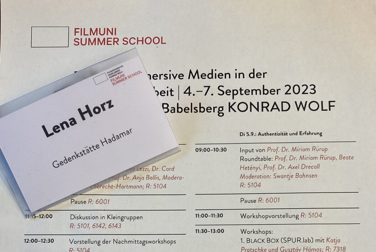 Ein Tagungsprogramm der Filmuni Summer School. Auf dem Plan liegt ein Namensschild, auf dem Lens Horz, Gedenkstätte Hadamar steht.