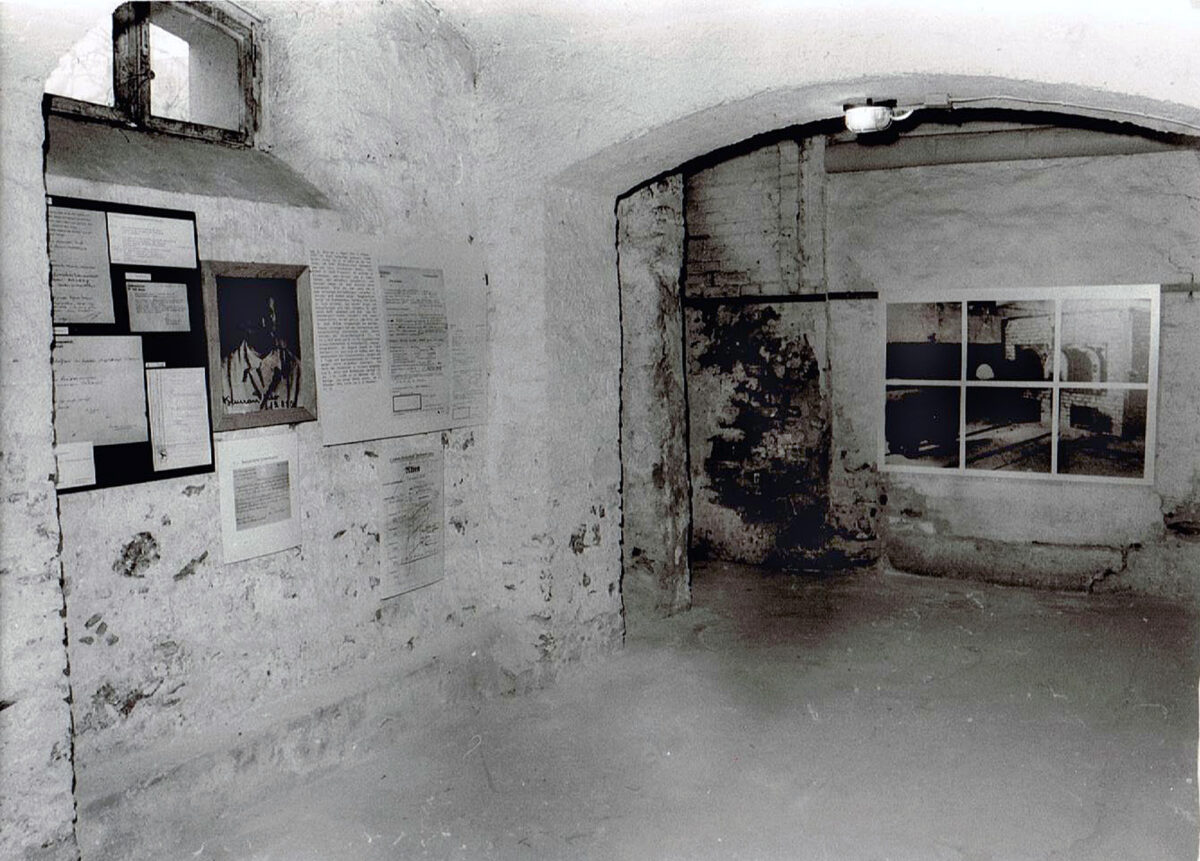 Ein schwarz-weiß Fotos eines alten Kellers. An den Wänden sind Ausstellungstafeln befestigt.